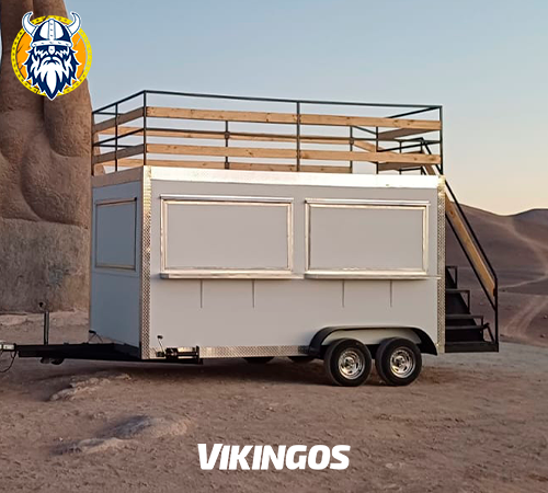 Carro con terraza de 2x4 metros, color base blanco, sobre la arena, con escalera lateral y sus ventanas cerradas